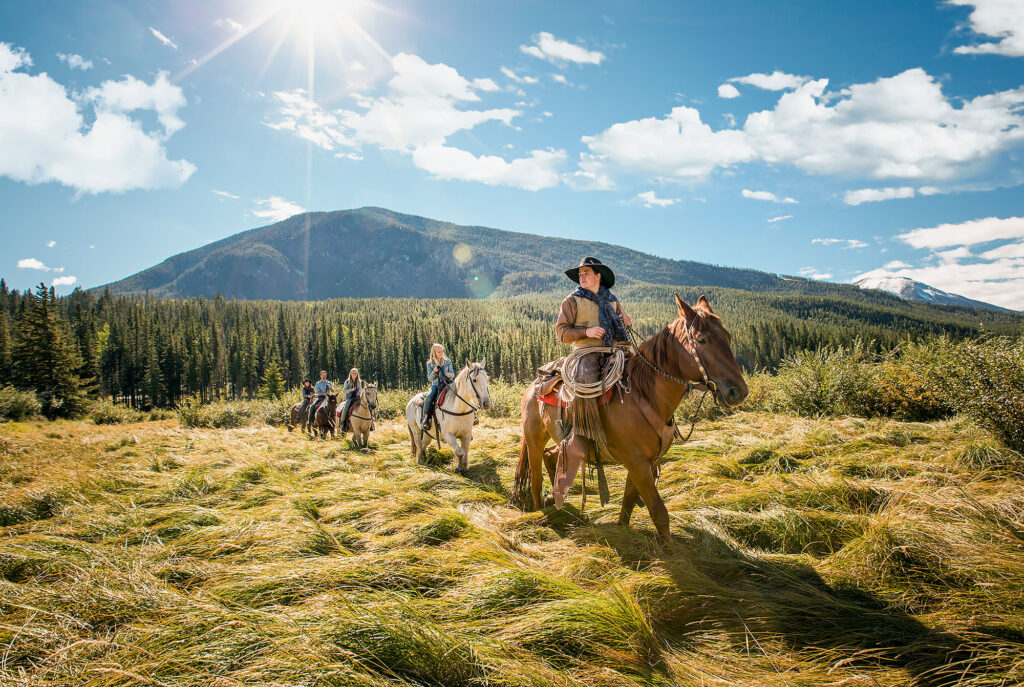 Cowboy leading a fall horseback trail ride under bluebird sky in Alberta.