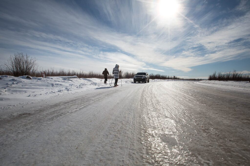 Snowshoers approaching an SUV travelling the ice road in northern Alberta